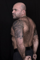 Big bald hairy powerlifter with polinesian tatoo on the shoulders