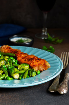 Baked salmon steak with asparagus, Brussels sprouts and green peas on a concrete background with a glass of wine.