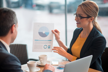 Side view happy businesswoman describing statistics to comrade. She keeping it in hand while...