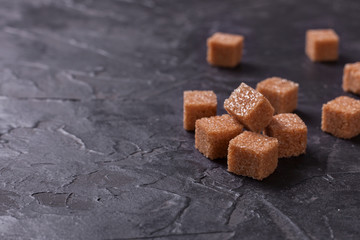 Brown cane sugar cubes pile on a black background. Copy space for text