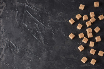Brown cane sugar cubes pile on a black background. Copy space for text