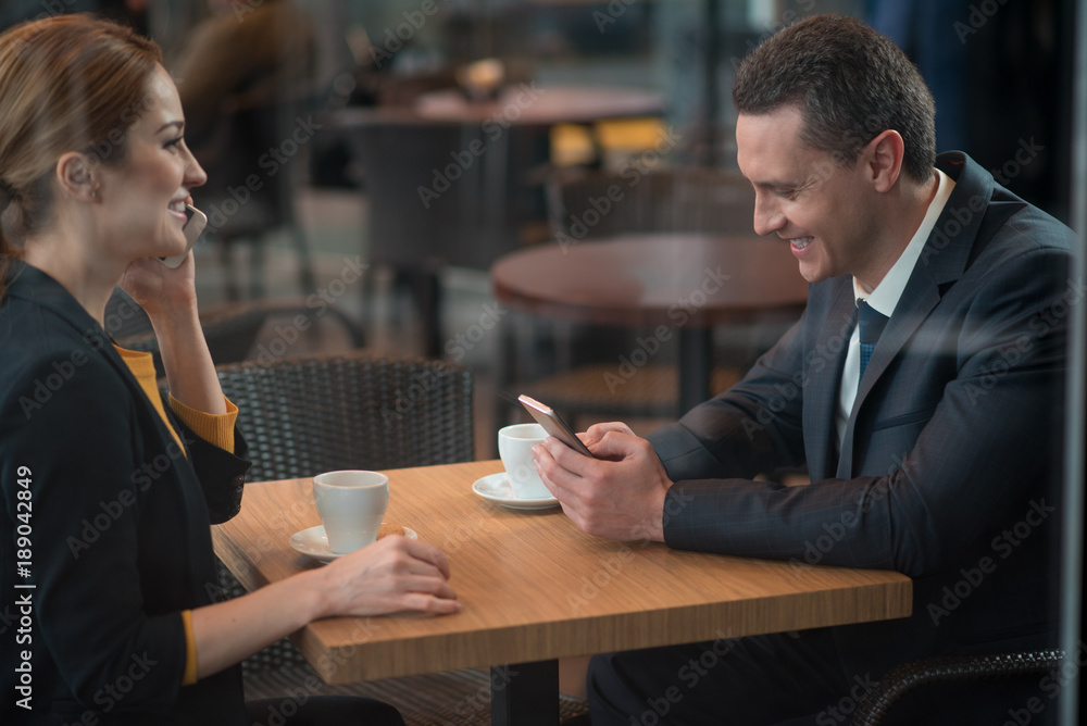 Poster side view cheerful man typing in mobile while sitting at table with partner. outgoing lady telling b