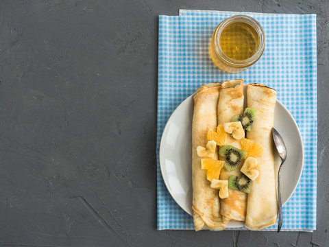 Delicious pancakes, decorated with pieces of banana, kiwi and orange, soaked in maple syrup