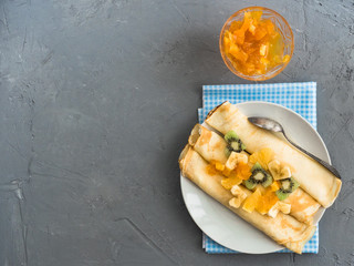 Delicious pancakes, decorated with pieces of banana, kiwi and orange, soaked in maple syrup