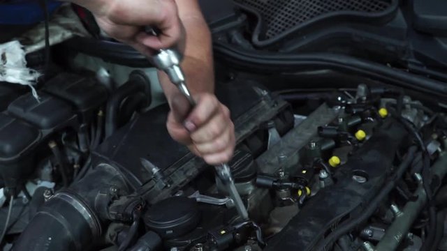 body shop. car engine repair. master unscrews the bolt under the hood
