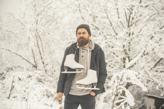 Bearded man smoking cigarette with skates in snowy forest.