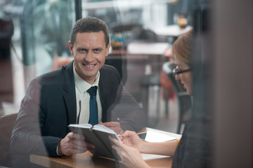 Portrait of beaming businessman talking with smiling female. He looking at camera while keeping...
