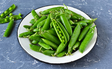 Fresh, young green peas in a plate on a concrete background. Bio food background.
