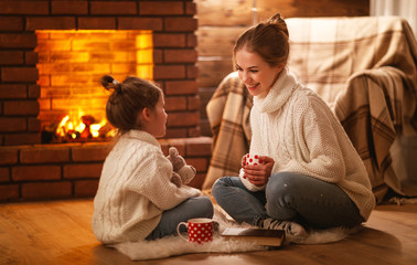 family mother and child drinking tea and laughing on winter evening by fireplace.