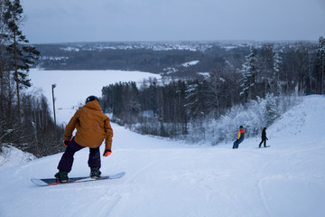 A snowboarder in an orange jacket starts to descend from the mountain