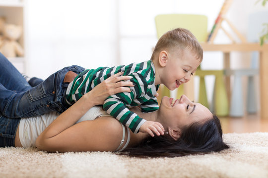 happy mother playing with kid on floor in children room