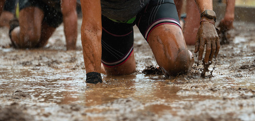 Mud race runners.Crawling,passing under a barbed wire obstacles during extreme obstacle race - obrazy, fototapety, plakaty