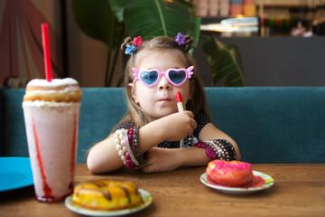 Adorable little girl with milkshake and dessert  in a cafe. The child sits at a table in a cafe. little girl as adult. children imitate adults.