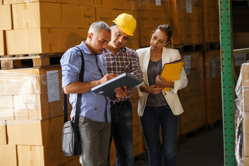 Two customs managers and warehouse worker checking list and inventory on the shelf in storehouse.