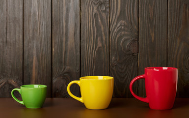 Different in size and color ceramic cups for coffee and tea - red, yellow and green on a dark wooden background.