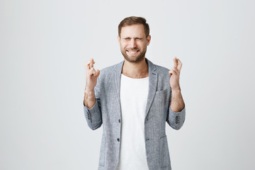 Handsome stylish bearded male entrepreneur with trendy haircut standing with crossed fingers and...