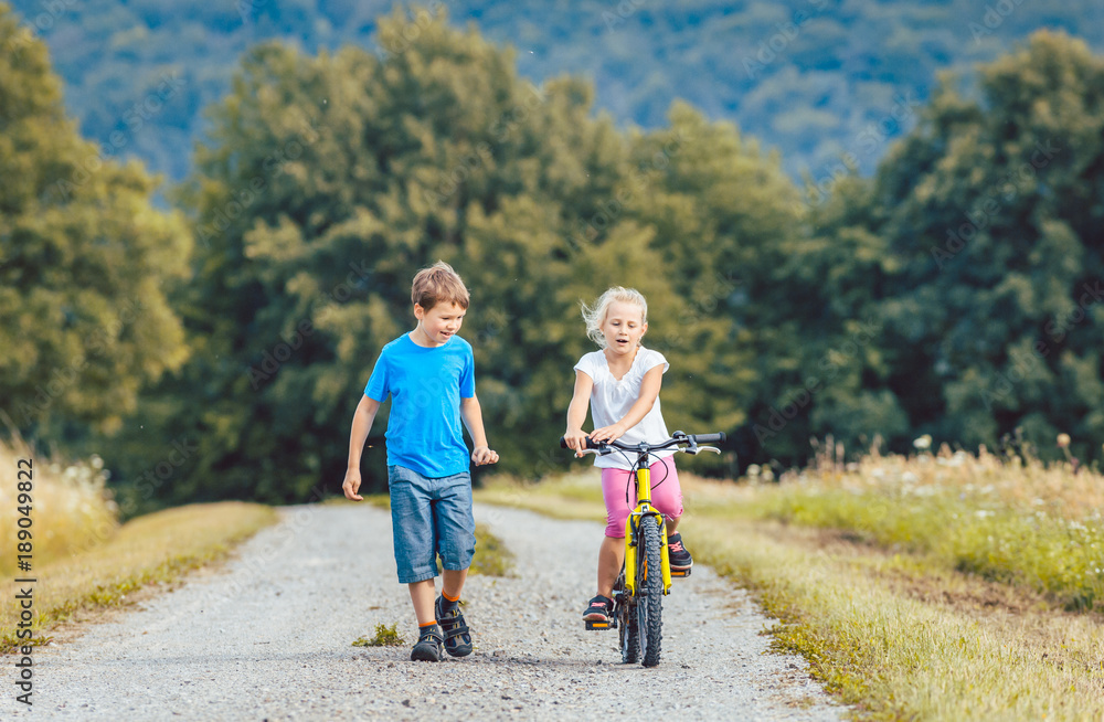 Poster kleiner junge und mädchen laufen und fahren fahrrad auf einem feldweg