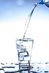Pouring water and splashing in the glass with reflection on mirror.