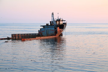 Unknown semi-submerged rusted and destroyed barge stranded in a bay