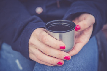 Junge Frau mit roten Fingernägeln hält Kafee (Thermobecher) in der Hand