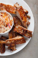 Grilled pork ribs in barbecue sauce and honey with sauerkraut on white plate. Snack to beer on a light stone table, Top view