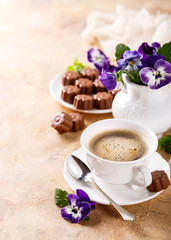 Holiday food composition with cup of cooffee, chocolate candies in flower shape and viola flowers. Postcard concept with copy space for text.
