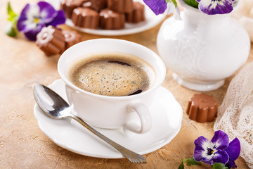 Holiday food composition with cup of cooffee, chocolate candies in flower shape and violets. Postcard concept.