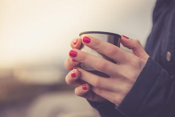 Junge Frau mit roten Fingernägeln hält Kafee (Thermobecher) in der Hand