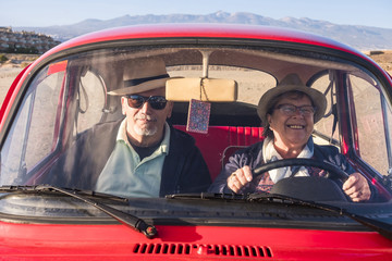 elderly couple with hats inside old red car