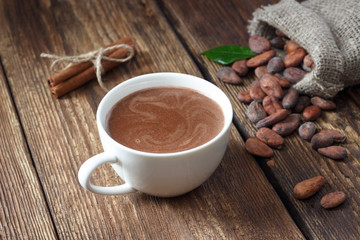 Cocoa drink in white mug and cocoa beans on wooden table.