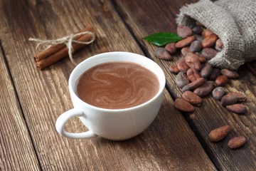 Fototapeten Kakaogetränk in weißer Tasse und Kakaobohnen auf Holztisch. © Dmitrii