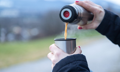 Junge Frau schenkt Kaffee aus Thermoskanne aus