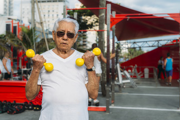 Older man (80-89) exercising using dumbbells at public gym in Ipanema, Rio de Janeiro, Brazil