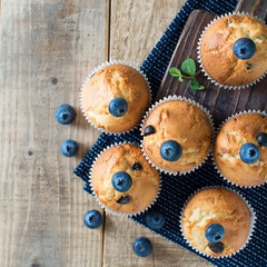 Blueberries muffins or cupcakes with mint leaves on wooden texture, square
