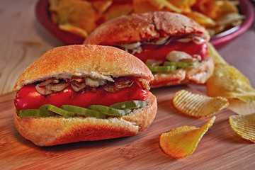 Grilled Hot dog or wiener with fried onions and marinated cucumbers. Potato chips. Ultimate classic fast food on wooden table.