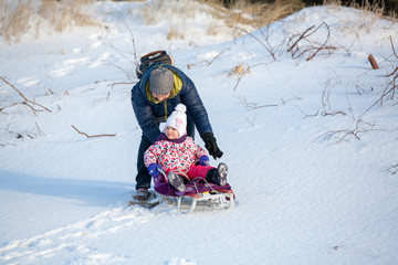 Fototapeta na wymiar Little girl child is towing with the sledge by gradmother in park in winter