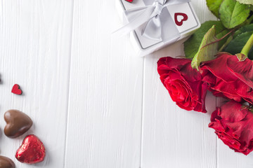 Valentines concept with bouquet of roses and wrapped gift on wooden table