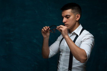 Portrait of serious young man in glasses and formal suit with suspenders on dark blue grunge background. Copyspace