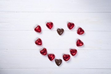 heart made of chocolates on white wooden background