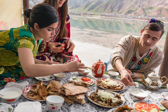 Women and man in traditional clothing of Tajikistan eating in restaurant by the lake
