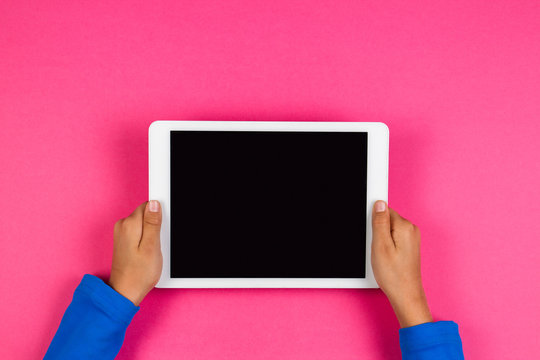 Kid hands with tablet computer on pink background.