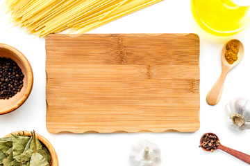 Cook a meal. Mock up for menu or recipe. Wooden cutting board near ingredients. Raw pasta, oil, garlic, spices on white background top view