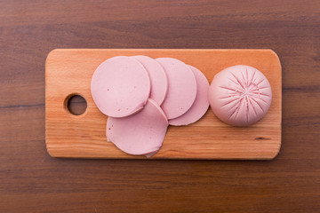 Sliced boiled sausage on cutting board on wooden table