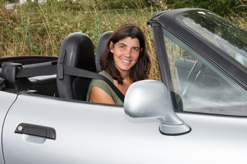 Pretty young brunette woman sitting at luxury grey cabriolet car