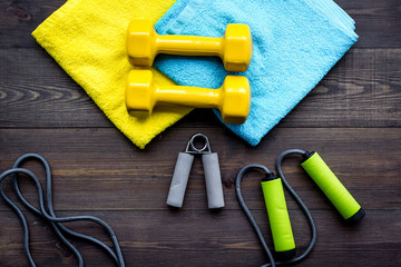 Fitness equipment. Dumbbells, expander, jumping rope on dark wooden background top view