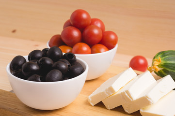 Greek salad with vegetables, feta cheese, black olives in process. Wooden background . Top view