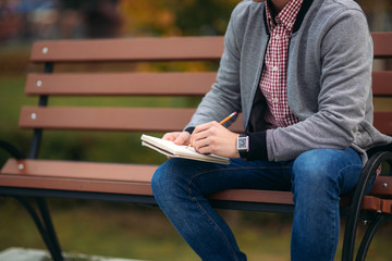 A cute student writes down his thoughts in his notebook using a pencil. Sits on bench