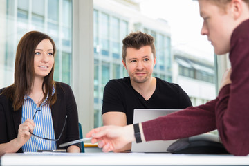 Business People Looking At Colleague Explaining At Desk