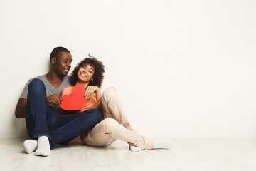 Fototapeta na wymiar Happy african-american couple in love holding red paper heart