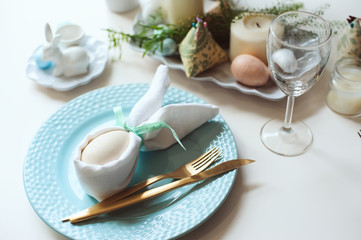easter festive table. Guest dining place decorated with bunny napkin and egg, golden metalic cutlery and blue plate